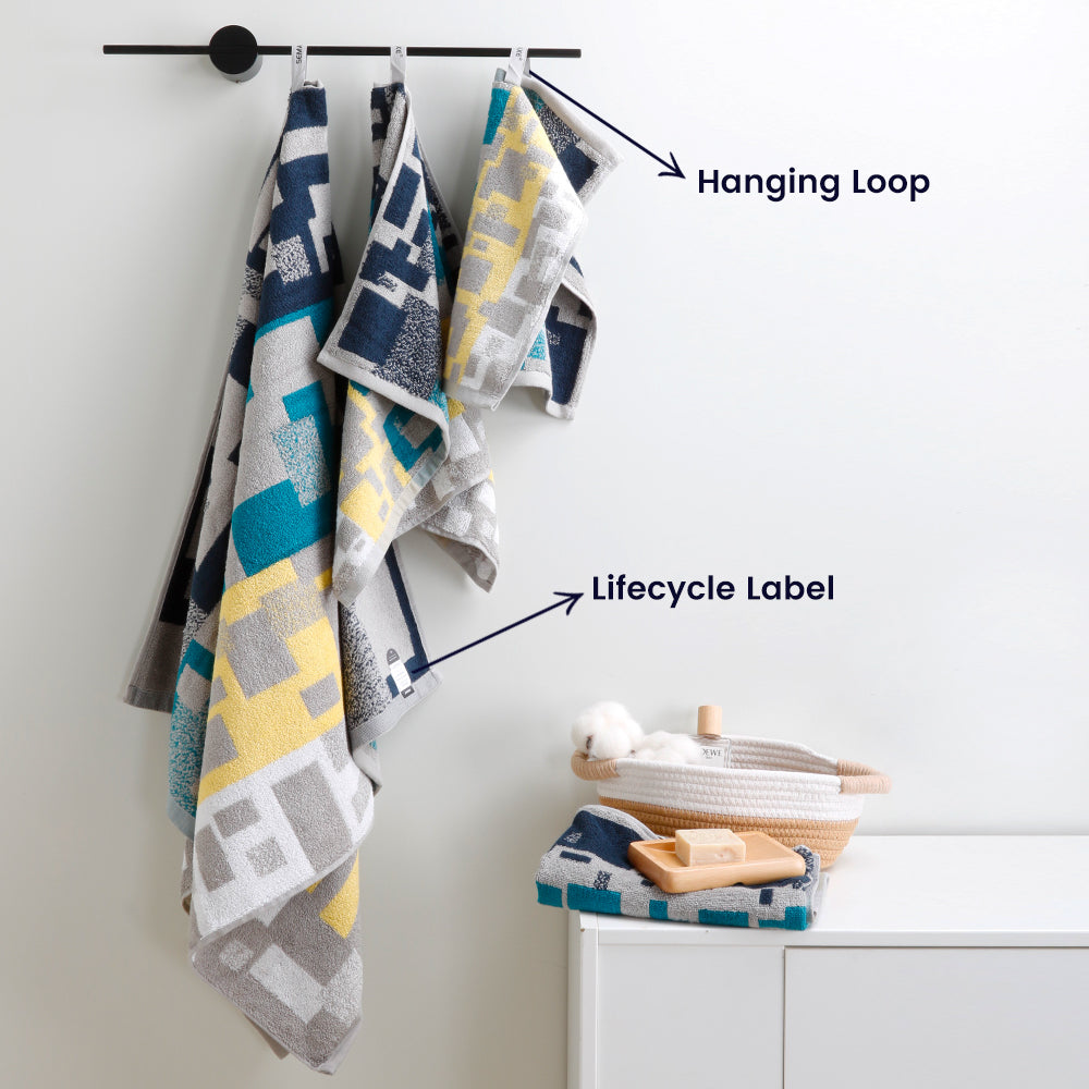 The "Impression" towel set with a geometric pattern hangs on the wall to easily display its unique hanging loop and lifecycle label