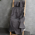 In the modern bathroom, there is a shelf full of charcoal gray towels