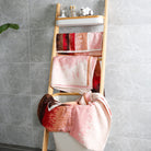 Bath towels and hand towels from the "Plum Garden" collection are hung on towel racks, revealing their distinctive red gradient pattern.