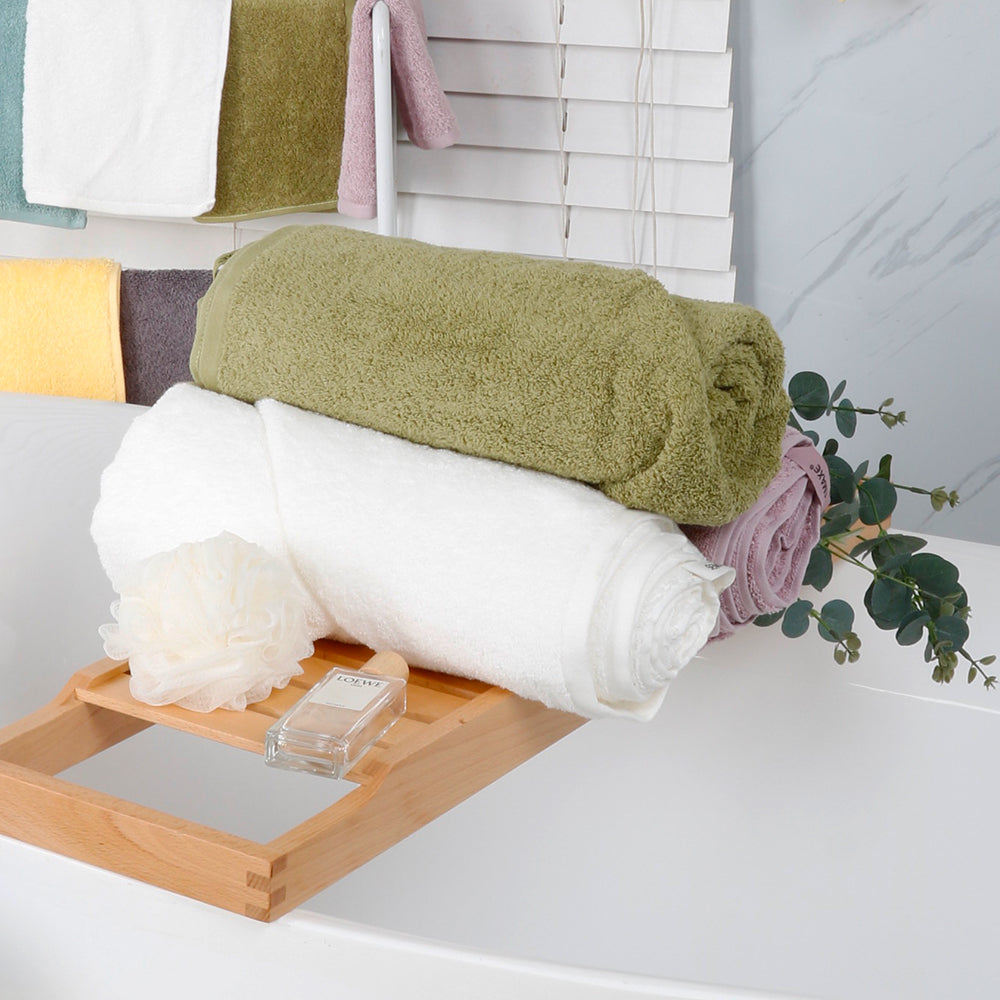 The bath towels from the Semaxe Plain collection are folded and placed on the bathtub shelf, showing off the green, white and purple colors of the collection