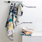 The "Impression" towel set with a geometric pattern hangs on the wall to easily display its unique hanging loop and lifecycle label